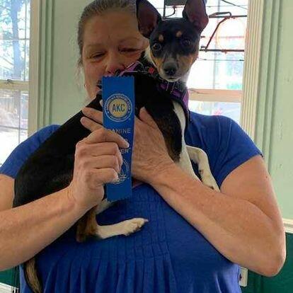 A woman is training a dog with a ribbon for dog obedience classes.