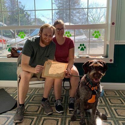 Two people and a dog posing for a photo during dog training class.