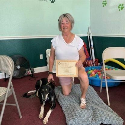A woman with a dog posing with a certificate from her dog training classes.